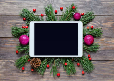 Christmas or new year background on a wooden background. Tablet with a blank screen for greetings. Flat lay, top view, copy spaceの写真素材