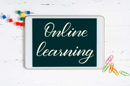 Online learning - handwritten inscription on a tablet. The concept of distance training for children. Tablet and office supplies on a white wooden background.の写真素材