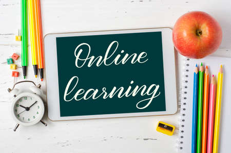 Online learning - handwritten inscription on a tablet. The concept of distance training for children. Tablet and office supplies on a white wooden background.の写真素材