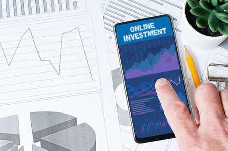 Online investment. A man is holding a smartphone with a mobile app with charts and graphs.