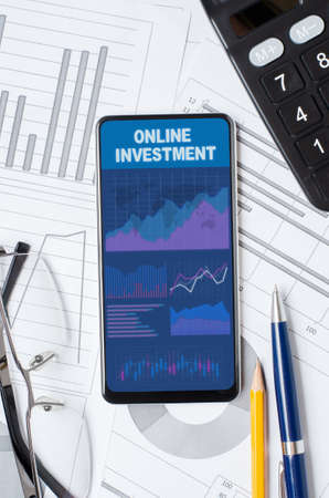 Online investment. Smartphone with a mobile app on the background of graphs and charts.の写真素材