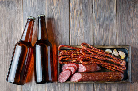 Ale in glass bottles and beer sausages. Brown wooden background. Copy space.の写真素材