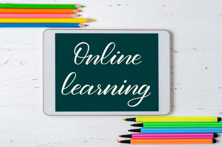 Online learning - handwritten inscription on a tablet. The concept of distance training for children. Tablet and office supplies on a white wooden background.の写真素材