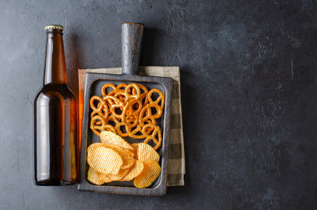 Beer in dark glass bottles and salty snacks. Dark concrete background. Top view. Free space for text.の写真素材
