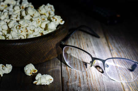 Popcorn, TV remote and glasses on a wooden background. Night. The concept of watching movies or TV series. Copy spaceの写真素材