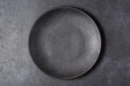 Dark grey textured concrete background for design with black food plate. Copy spaceの写真素材