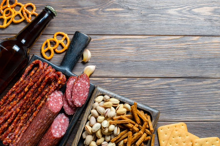 Beer in dark glass bottles, salty snacks for beer, sausage. Brown wooden background. Drinks and food for a drunken party. Copy space.の写真素材