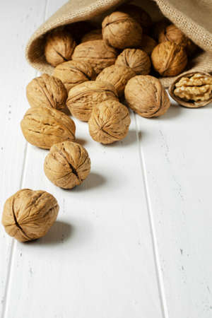 Lots of walnuts in a burlap bag. Wooden white background. Copy space