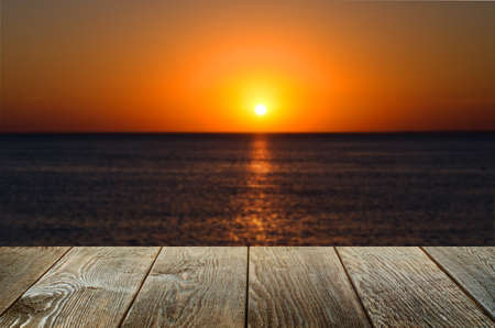 An empty brown wooden table. Blurred background with sunset on the sea.の写真素材