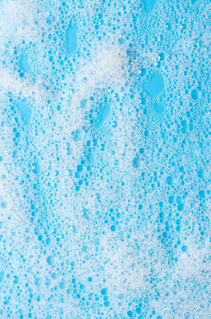 Texture of white foam on a blue background. Cleansing mousse for the face or bath foam or washing powder. Closeupの写真素材
