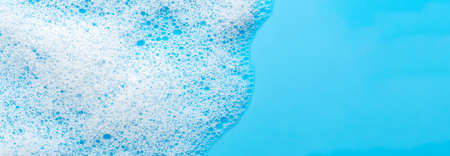 Texture of white foam on a blue background. Cleansing mousse for the face or bath foam or washing powder. Closeup. Copy spaceの写真素材