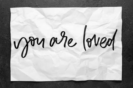 You are loved. Lettering on crumpled white paper. Handwritten text. Inspirational quotes.の写真素材
