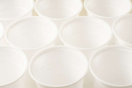 Disposable white plastic tableware on a beige background. The concept of nature pollutionの写真素材