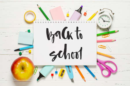 Childrens accessories for study, creativity and office supplies on a white wooden background. Handwritten inscription Back to school on a white notebook.の写真素材