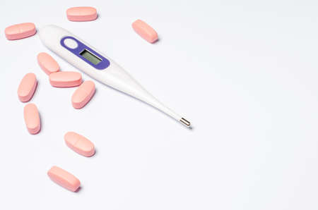 Medical electronic thermometer and tablets on a white background. The concept of diagnosis and...