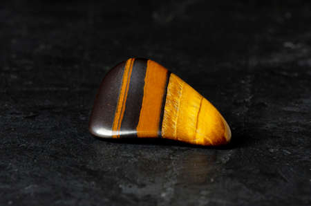 Tigers eye mineral on a black concrete background. The concept of using minerals and crystals in...