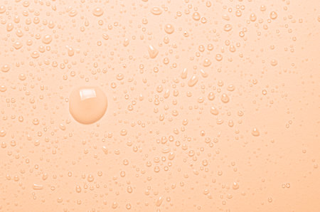 Drops of micellar water or cosmetic tonic on an orange background. Close-up, macro photographyの写真素材