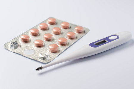 Medical electronic thermometer and tablets on a white background. The concept of diagnosis and...