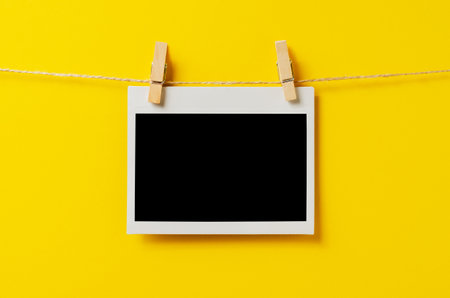 An empty photo is hanging on a rope with a clothespin. A design element. Yellow background. Copy space.の写真素材
