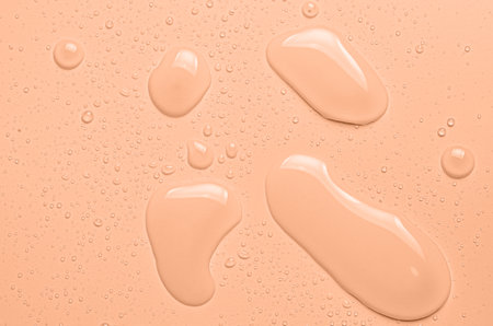 Drops of micellar water or cosmetic tonic on an orange background. Close-up, macro photographyの写真素材
