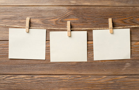 Empty paper sheets hang on a rope. A design element. Brown wooden background. Copy space.の写真素材