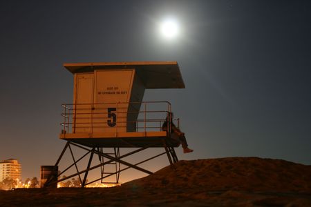 The moon rises over a life guard tower at a beach where two lovers enjoy the eveningの写真素材