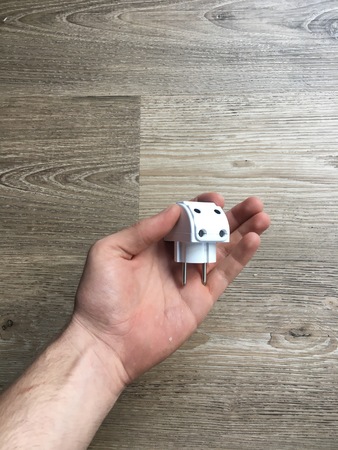 hand holding a white multiplug above a wooden deskの写真素材