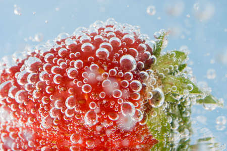 Strawberry submerged in bubbly soda against a blue background