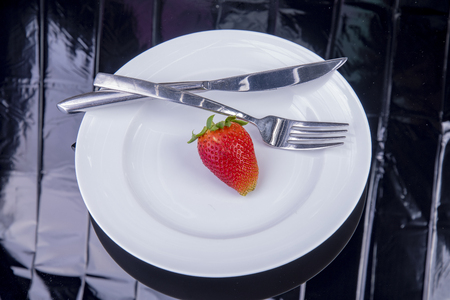 single strawberry with knife and fork on a white plateの写真素材