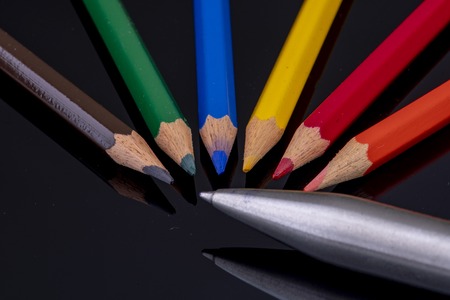 the tips of coloured wooden pencils on a black background with mirror image versus ballpoint pen