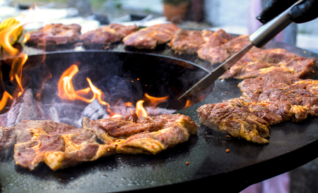 barbeque with fresh bloody steaks and open fire and the hand of a catererの写真素材