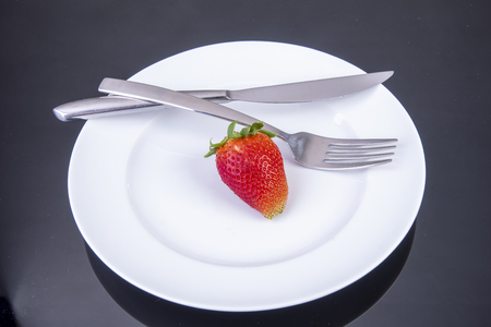 single strawberry with knife and fork on a white plateの写真素材