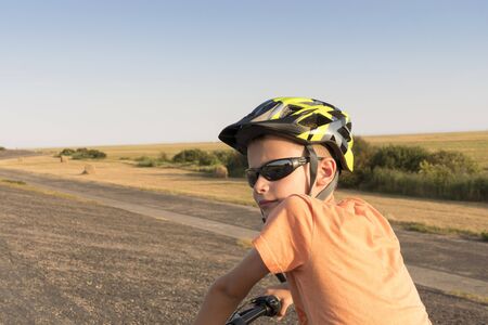 a young boy riding alone on a bicycle on the dam at the North Sea between high reed grassの写真素材