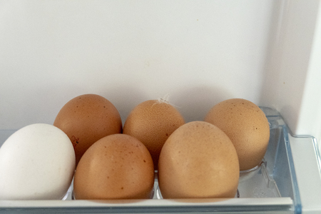 brown and white eggs in fridge with small featherの写真素材