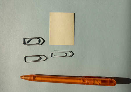 attached yellow note with paperclips and orange pen on blue background