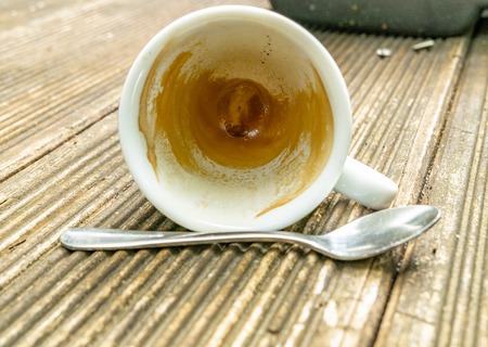 tilted dirty empty espresso cup on a wooden table with coffee crema and spoonの写真素材