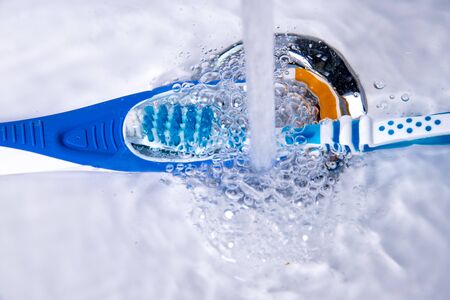 tongue cleaner and toothbrush under running water in the bathroomの写真素材