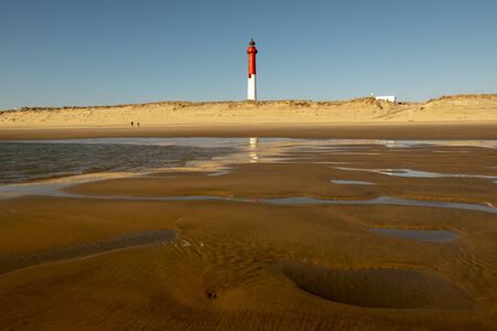 Sunset at low tide with red and white lighthouse on the beachの写真素材