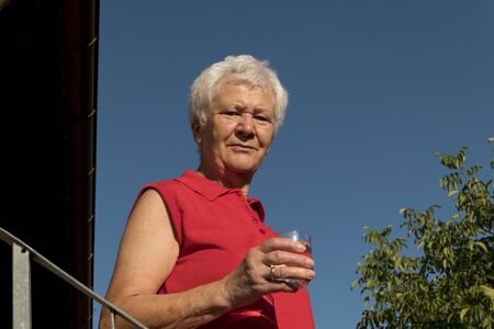old lady drinking a glass of water in front of a blue sky