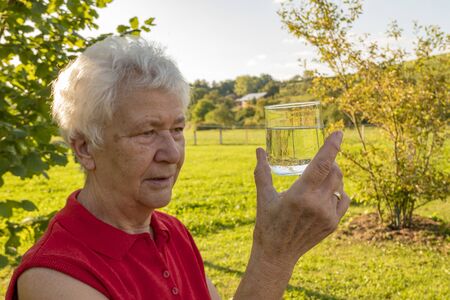 Senior citizen enjoys testing a glass of water in the gardenの写真素材