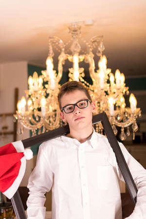 Boy with glasses and white shirt in front of festive candlestick and Christmas hatの写真素材