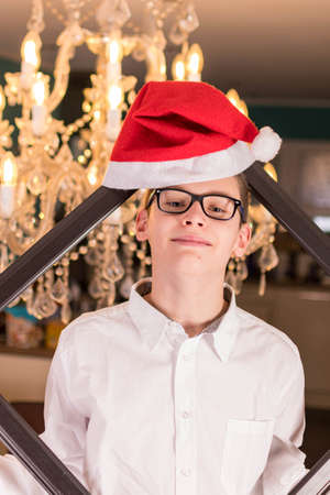 Boy with glasses and white shirt in front of festive candlestick and Christmas hatの写真素材