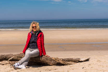 Blonde woman sitting in the wind on a tree on the beachの写真素材