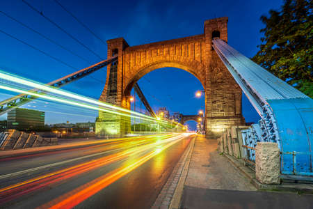 Grunwald Bridge. Grunwaldzki suspension bridge in Wroclaw, Poland at dusk with fast moving cars, trams creating traffic light trails. The most known city landmark seen from the bank sideの写真素材