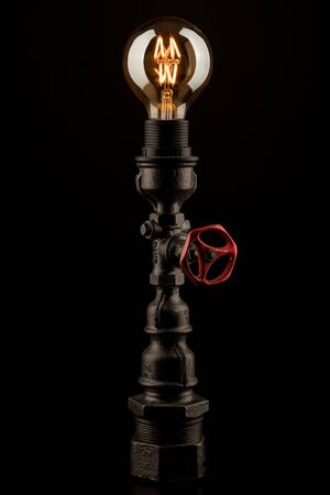 Vintage lamp made from steel water pipe fittings with lit filament bulb and valve switch, on black backgroundの写真素材