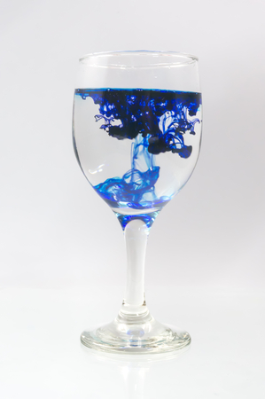 Glass full of water with ink color dropの写真素材