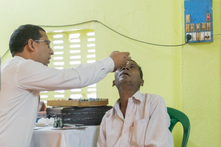 KOLKATA , INDIA - MARCH 19, 2017 : Male Doctor eye specialist checking eye sight of adult male sitting on a chair, at a free public eye testing camp. Editorial stock image.のeditorial素材