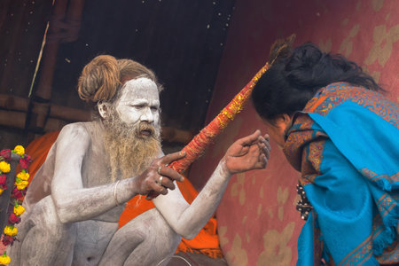 BABUGHAT, KOLKATA, WEST BENGAL / INDIA - 11TH JANUARY 2015 : Hindu Sadhu with white ash applied on body and face, blessing blue sari clad Indian devotee woman.のeditorial素材