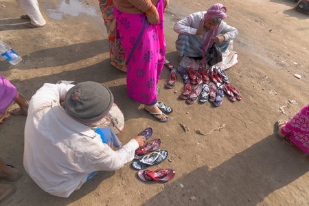 KOLKATA, WEST BENGAL , INDIA - JANUARY 18TH 2015 : A seated Indian male selling colorful chappals (shoes) to sari clad standing Indian women, Indian ladies prefer such casual shoes.のeditorial素材