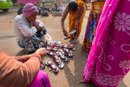 KOLKATA, WEST BENGAL , INDIA - JANUARY 18TH 2015 : A seated Indian male selling colorful chappals (shoes) to sari clad standing Indian women, Indian ladies prefer such casual shoes.のeditorial素材